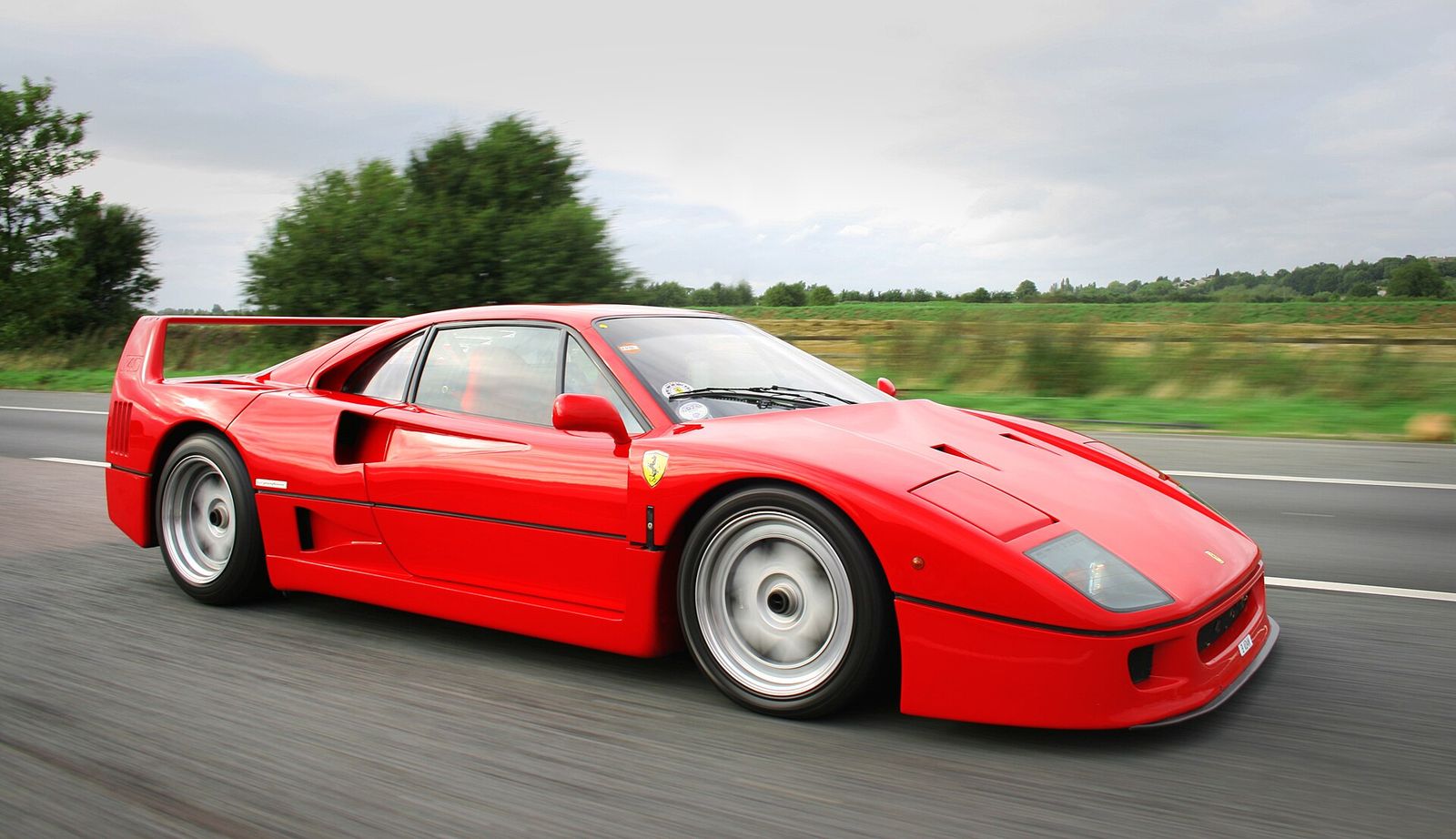 Red Ferrari F40 driving along a country road, seen from the side